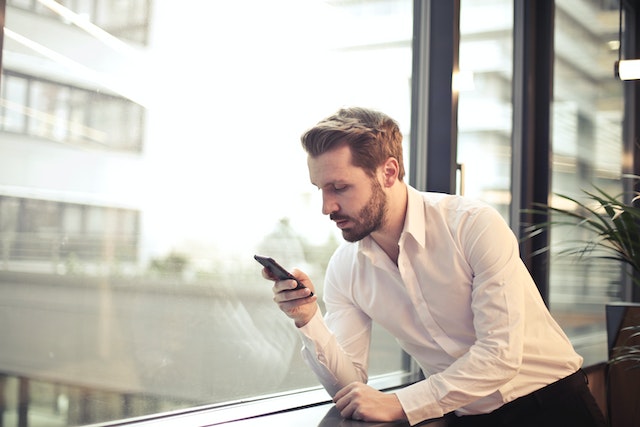 a landlord in a white button down shirt sits by a window and texts their tenant to remind them of seasonal maintenance responsibilities